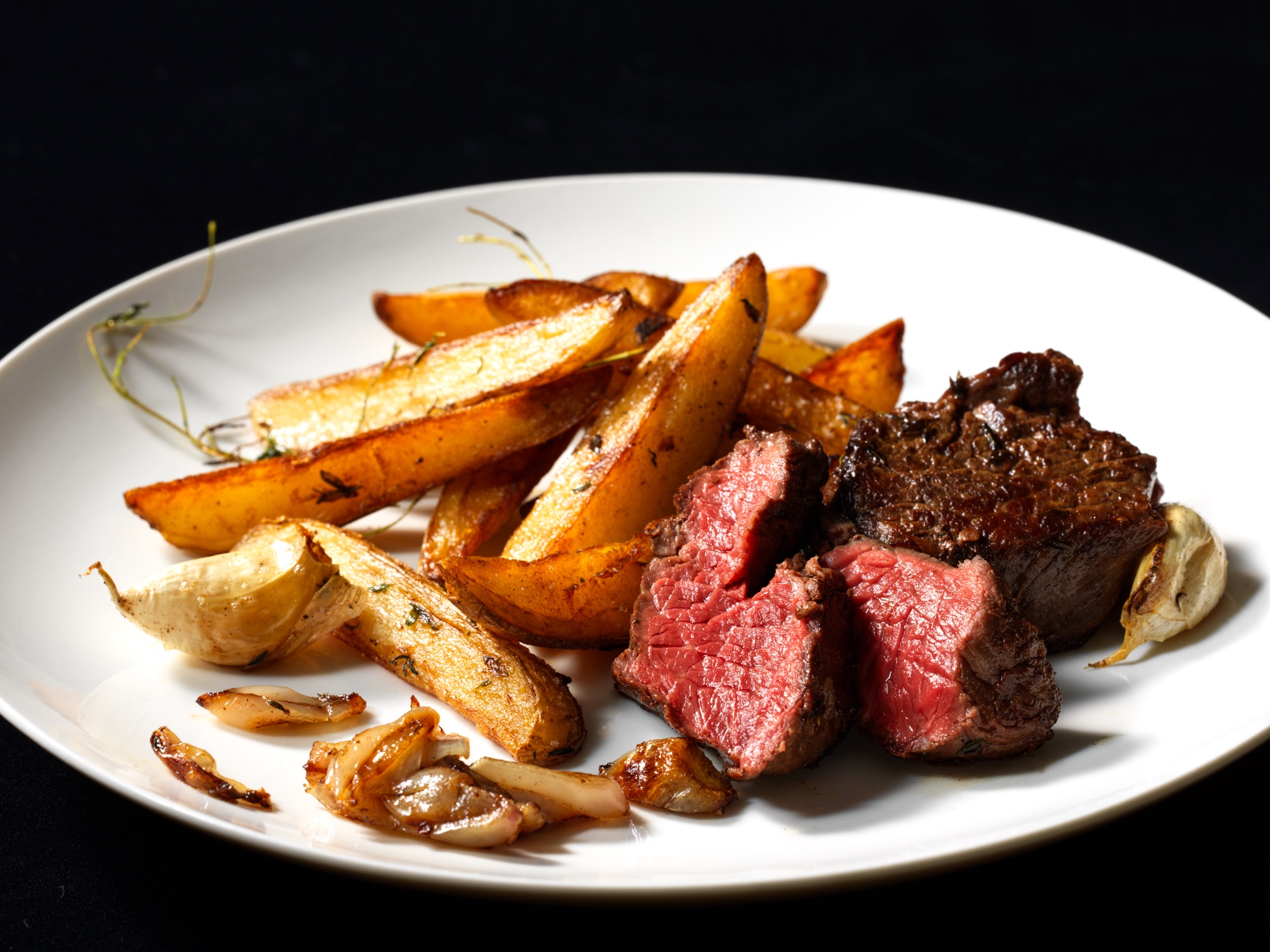 岩手短角牛のステーキとフライドポテト。黒バックに白皿、断面の赤さを見せたシズルカット